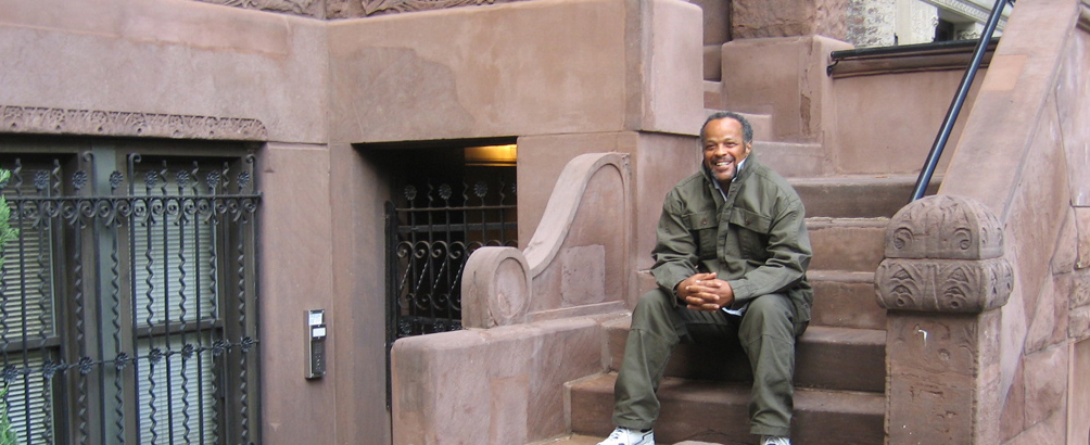 Middle aged man in green tracksuit sitting on steps of a brownstone.