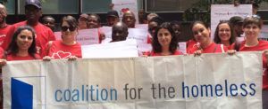 Men and women in red shirts holding posters and the Coalition for the Homeless banner.