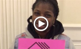 A woman in a black hoodie and jean jacket holding a pink House Our Future NY sign. A play button indicates video.