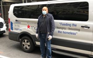 man in mask in front of white van with letters saying feeding the hungry housing the homeless