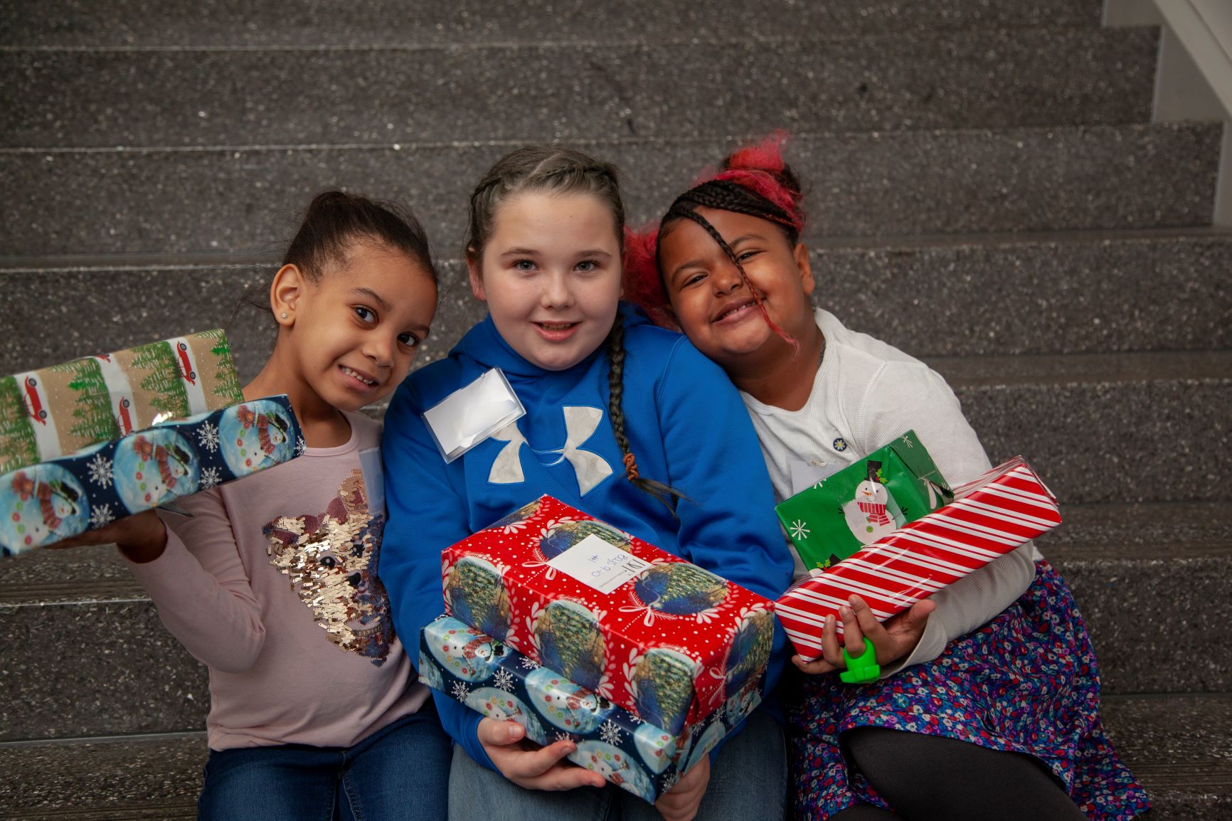 Three children holding brightly wrapped gifts.