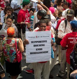 A man holds a sign in a crowd that says "Supportive Housing Ends Homelessness"