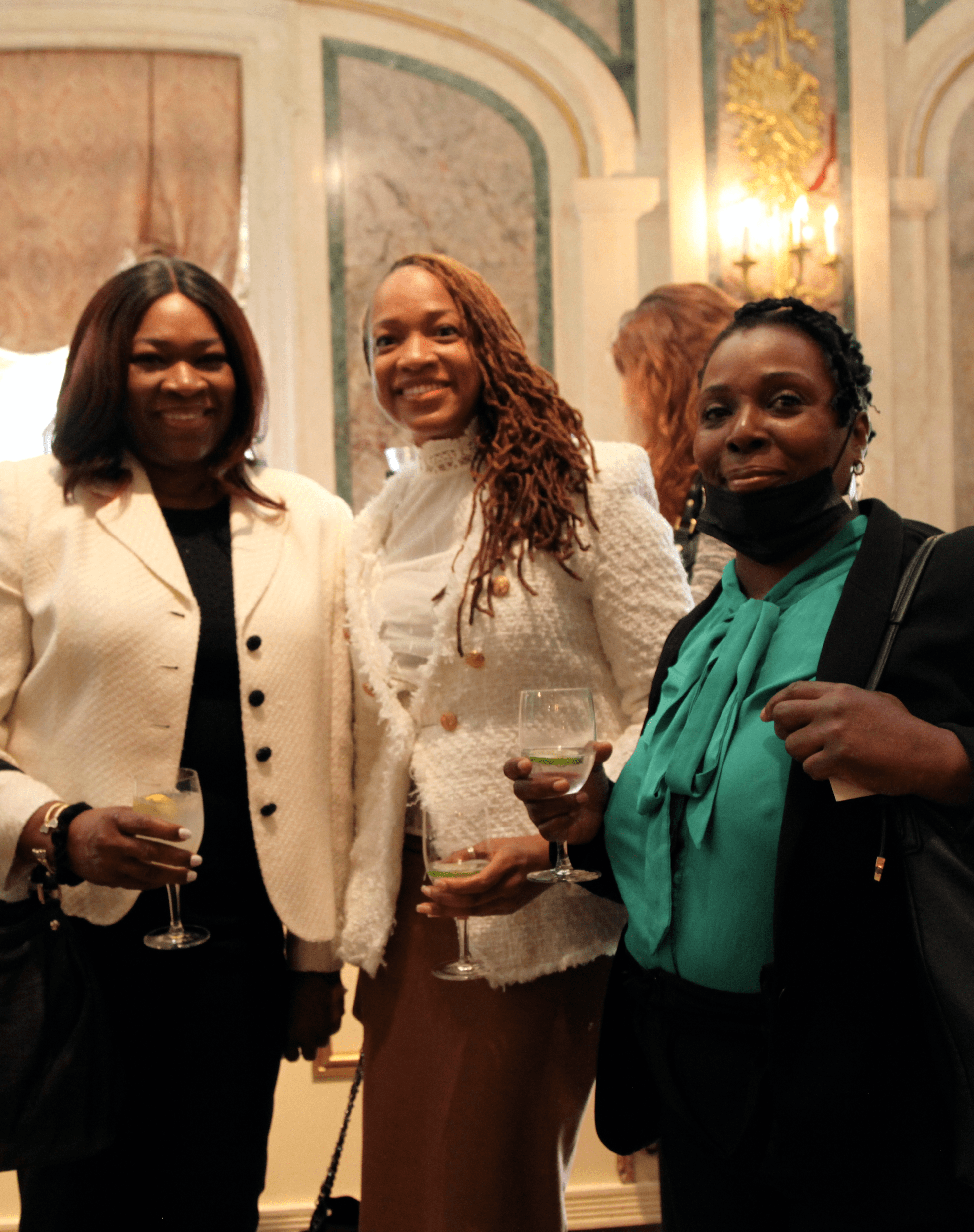 Three women stand in the lobby of the Plaza Hotel's Grand Ballroom and smile at the camera.
