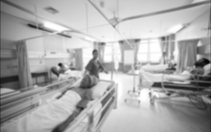 A blurred black and white photo inside a hospital room with 3 patients and a nurse.