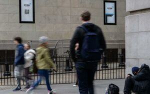 A blurred image of people walking in the streets of NYC and a homeless person slouched over on the floor.