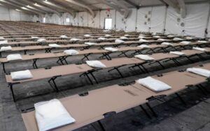 Rows of cot beds with a pillow inside a facility.