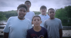 A still of a video of boys speaking to camera, standing in front of a lake.