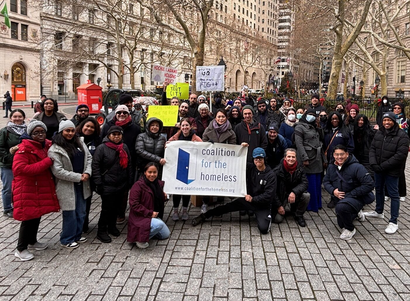 A group of people grouped together, smiling at camera and holding a sign that reads "Coalition for the Homeless" suggesting this is a staff photo.