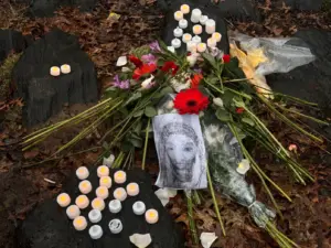 An image of flowers and candles gathered underneath a tree with a hand-drawn picture of a man, suggesting a memorial for this person.