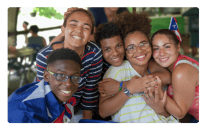 A group of kids embrace and smile at camera. They are in summer clothing.
