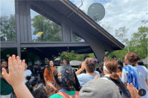 A group of kids singing outside an open-air dwelling.