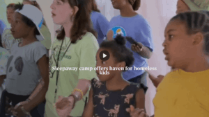 A group of kids dressed in colorful clothing, singing. Text overlaid reads "sleepaway camp offers haven for homeless kids".