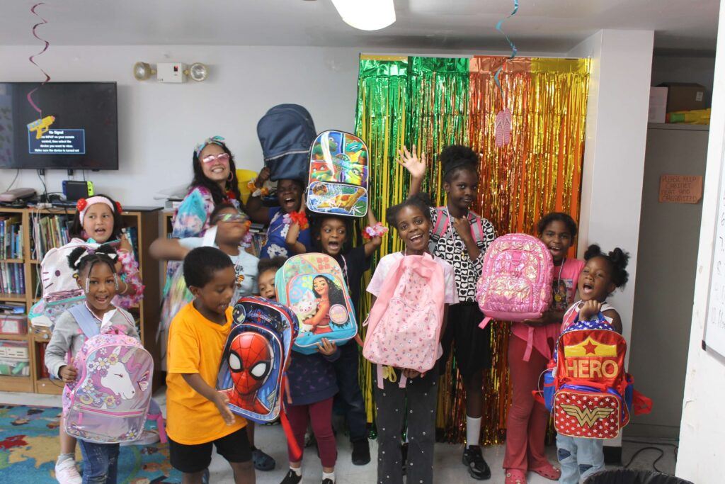 Kids holding new, backpacks smiling and waving at the camera.