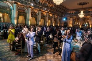 An ornate ballroom; guests are standing and applauding.